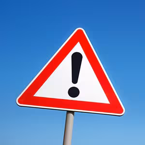 Warning sign on post outside against blue sky.