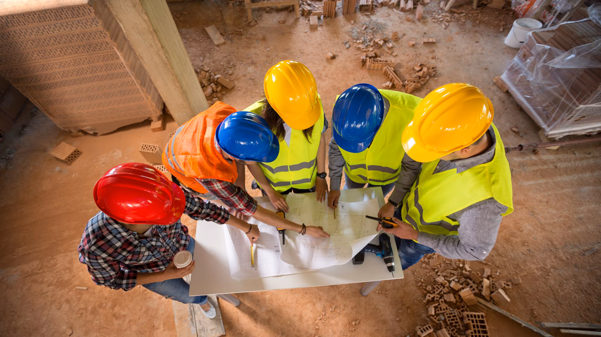 five people in hard hats standing looking at plans together