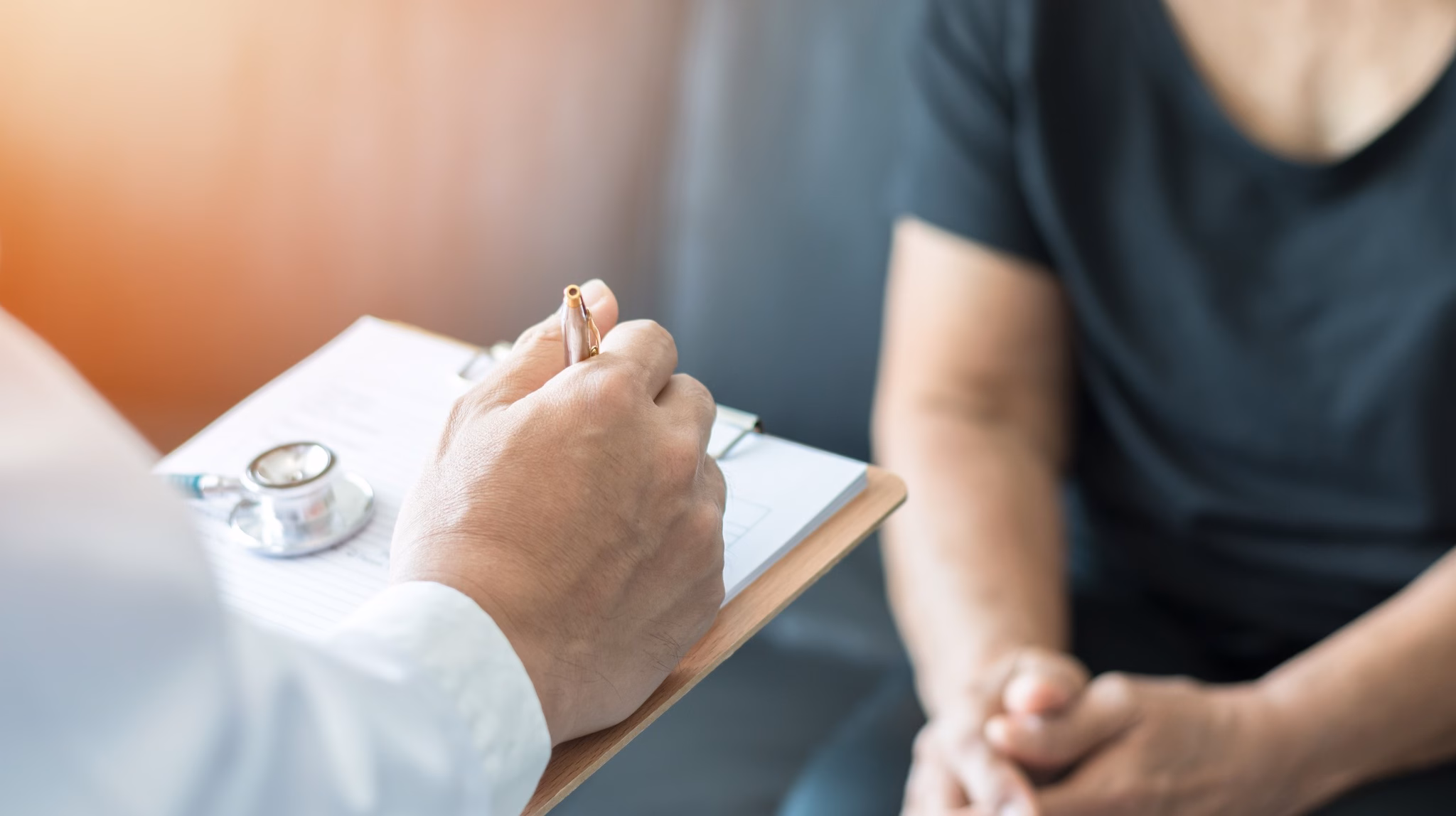 Doctor consultation Clinician hands writing on a clipboard standing in front of someone sitting down