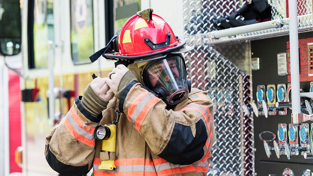 — title missing — Firefighter in full gear strapping on a respirator in front of a fire truck.