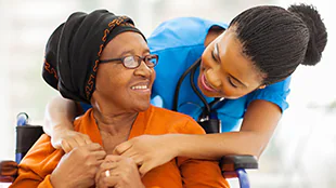 An older woman is embraced from behind by a medical professional