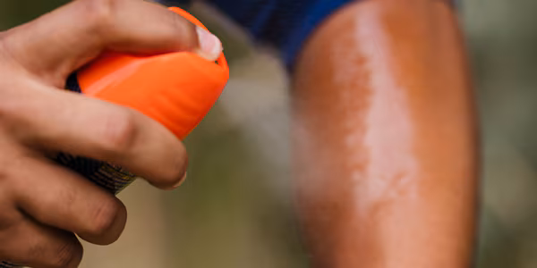 Person spraying insect repellent onto their arm