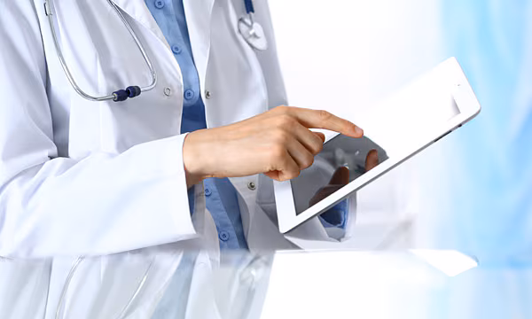 Health Care Worker Utilizing Technology A close up photo of a person wearing a lab coat and holding and tablet computer.
