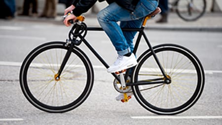 urban-biker-bikepage A cyclist wearing jeans and sneakers riding a bicycle