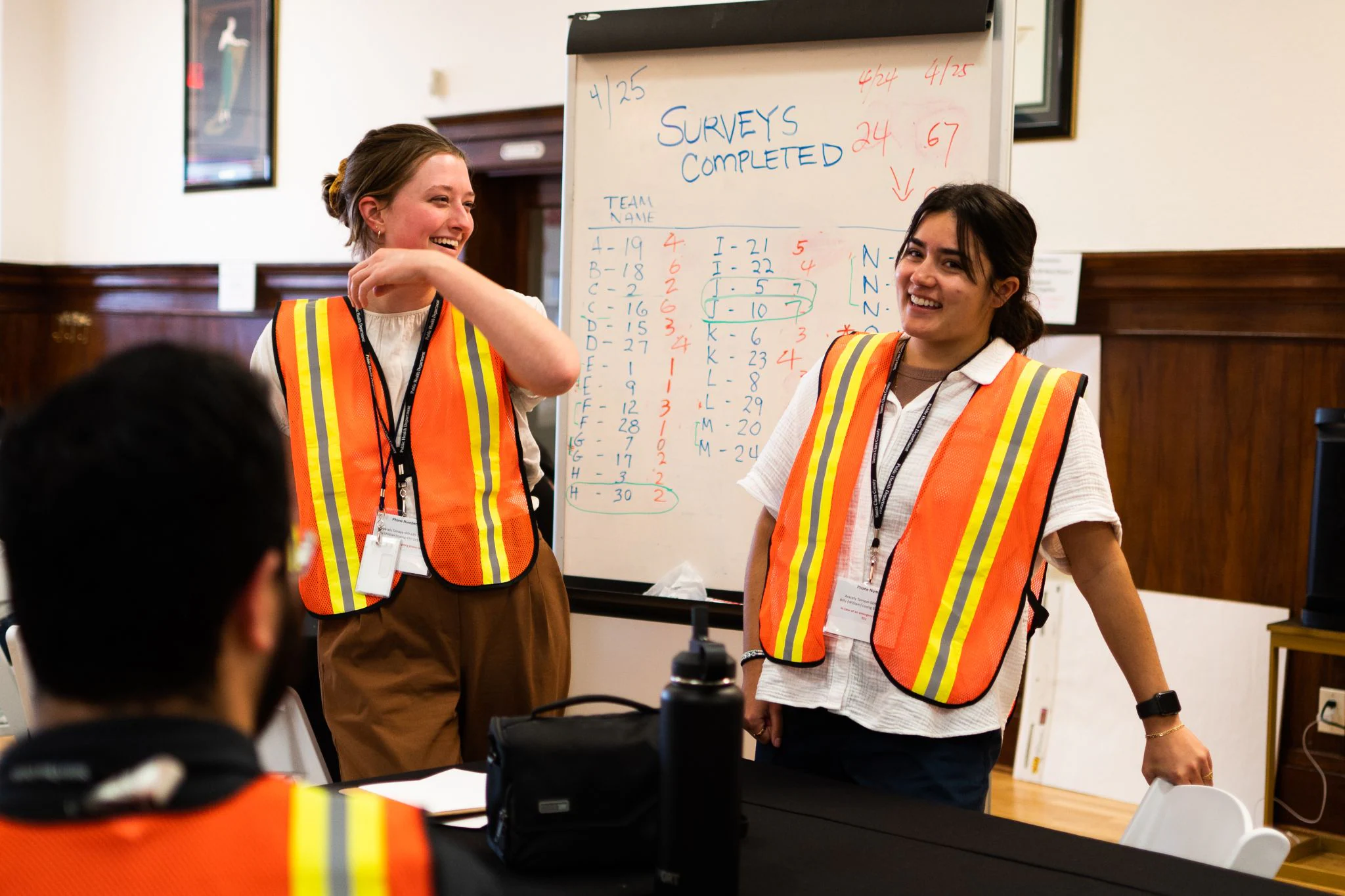 PHAP_CASPER24 Two Public Health Associates wearing high-visibility reflective vests smile while presenting survey data to colleagues.