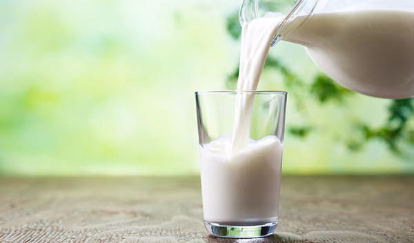 Pitcher pouring milk into a glass on a table.