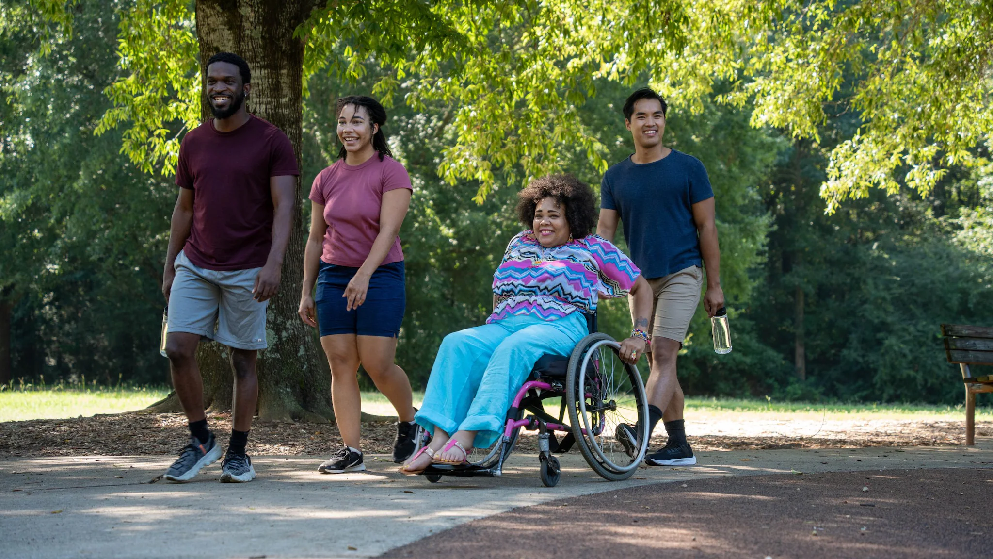 — title missing — A diverse group of young people walking and rolling a wheelchair through a park