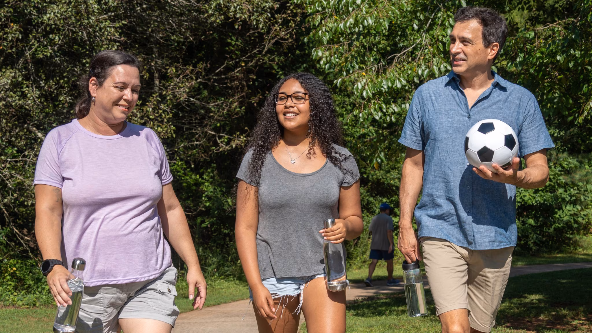 Family walking in the park with a soccer ball.