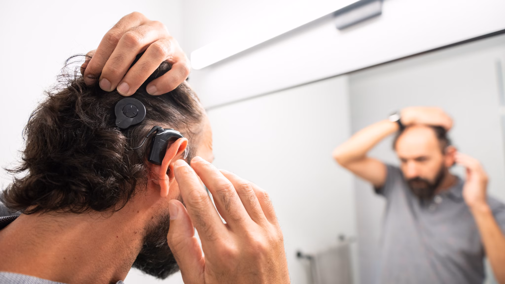 Man adjusting his cochlear implant in the mirror in his home bathroom.