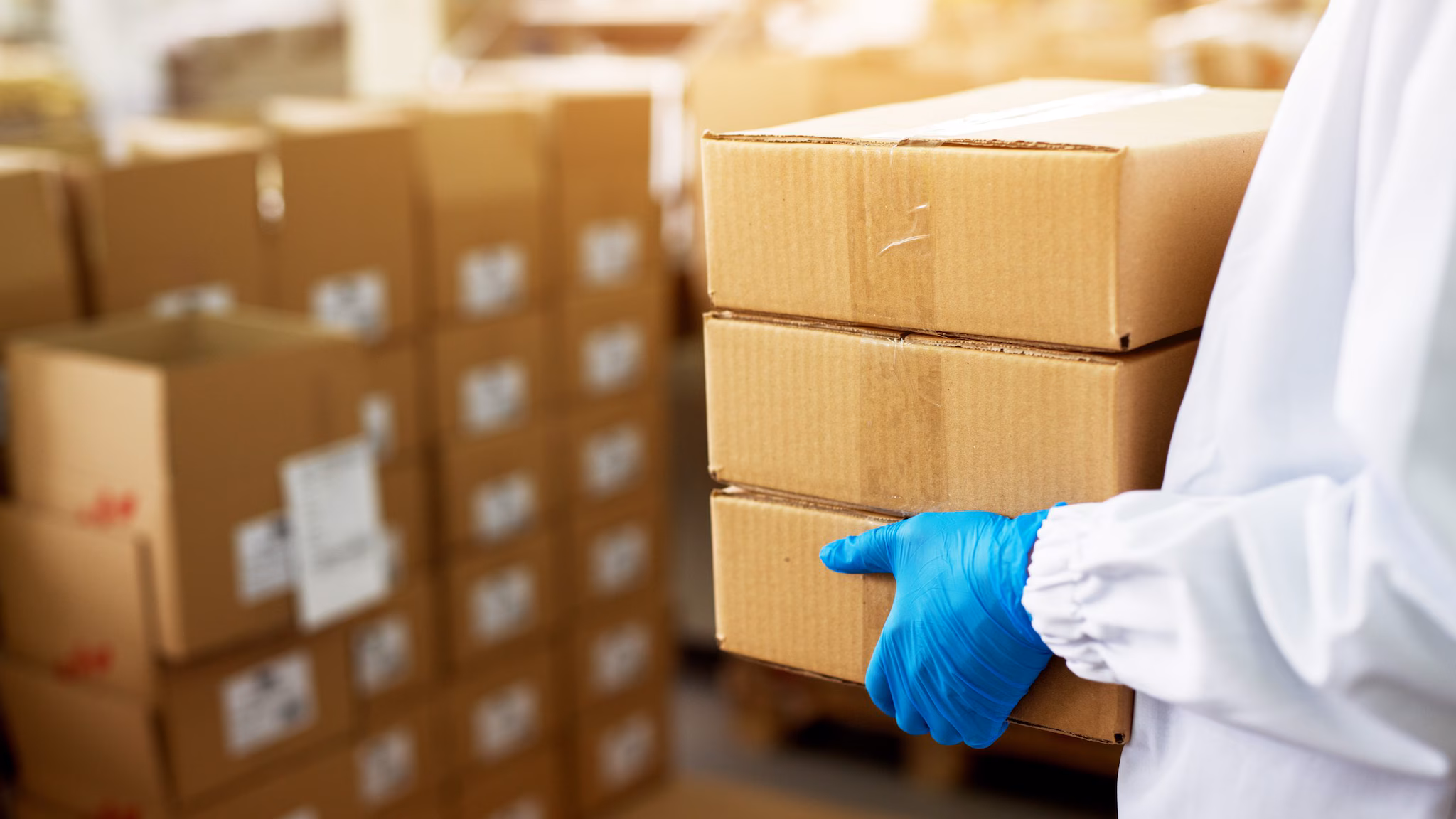 submitting specimens for testing Person wearing a lab coat and blue gloves carrying cardboard boxes.