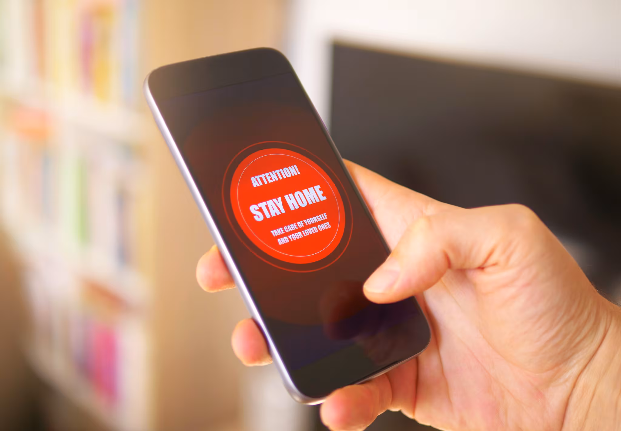 Red emergency alert on a black cell phone screen reads "stay home - take care of yourself and loved ones"