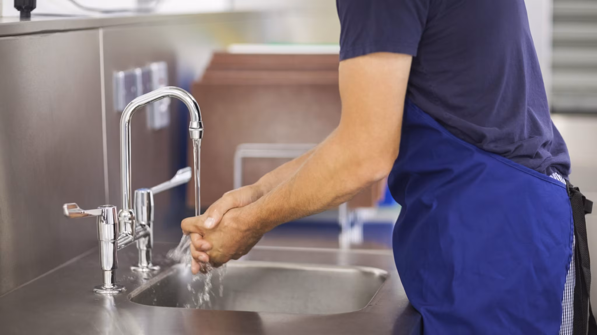 Person washing their hands at a restaurant kitchen sink.