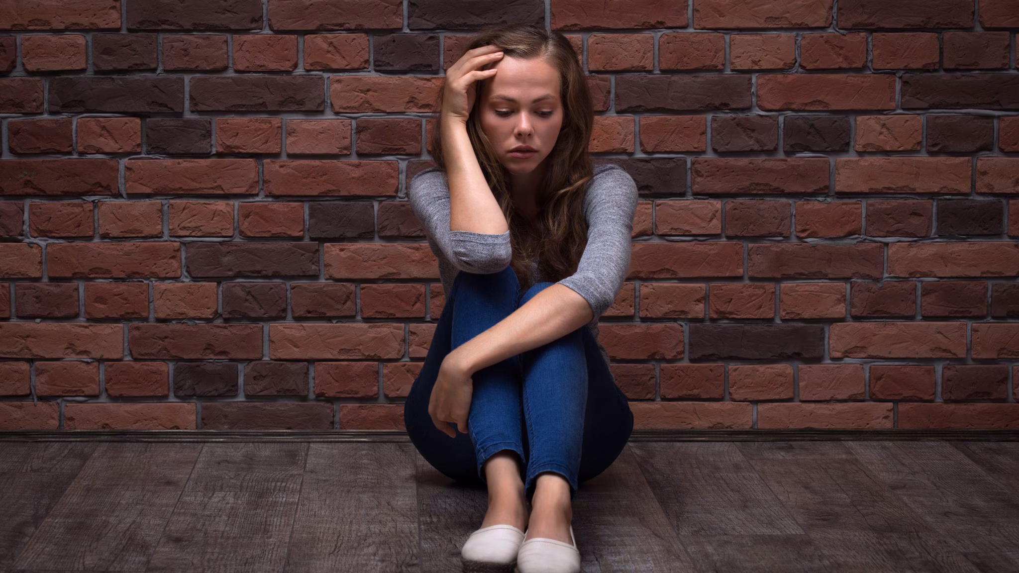 Depressed Teenager Girl Sitting against a brick wall