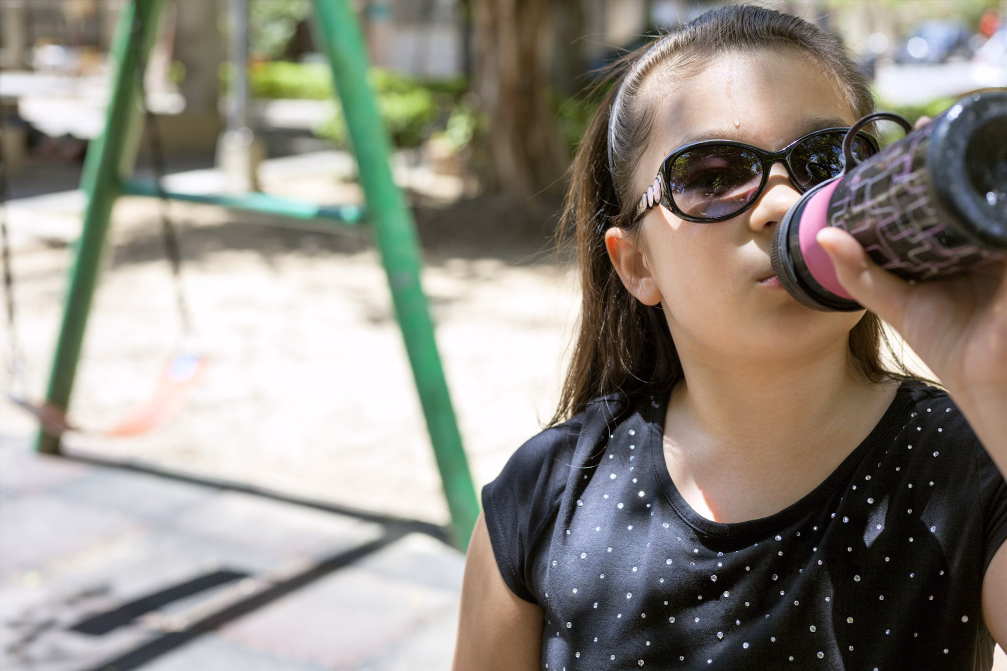 Drink Water A young girl drinking from a water bottle in a playground.