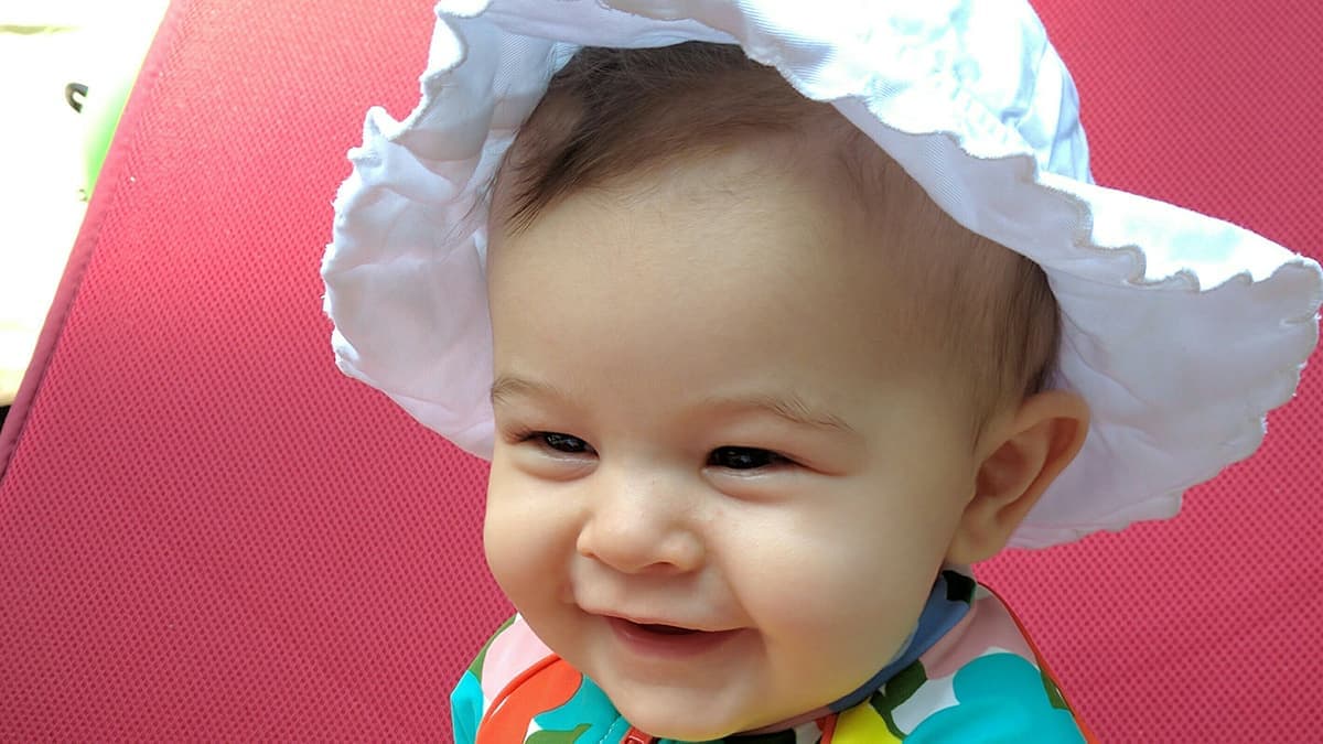 Child wearing sun protection gear sitting in a chair.