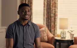 video4 Black male sitting in room with window and chair behind him talking to camera