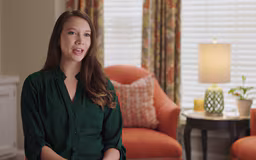 video6 White female sitting in room with window and chair behind her talking to camera