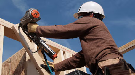 — title missing — A construction worker uses a nail gun to build a house.