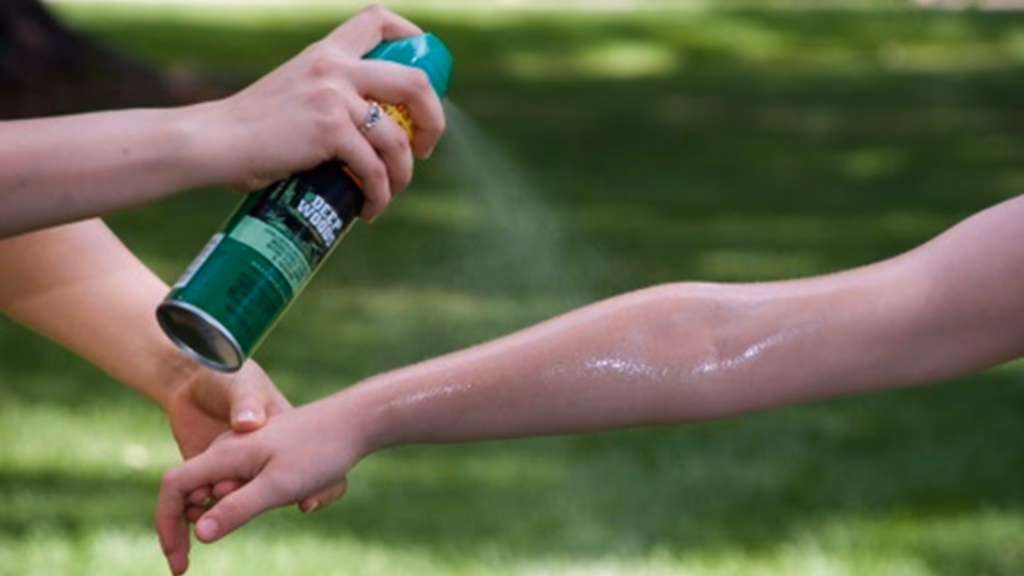 Person spraying insect repellent on another's arm