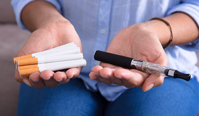 Woman holding cigarettes in one hand and an e-cigarette in the other hand.