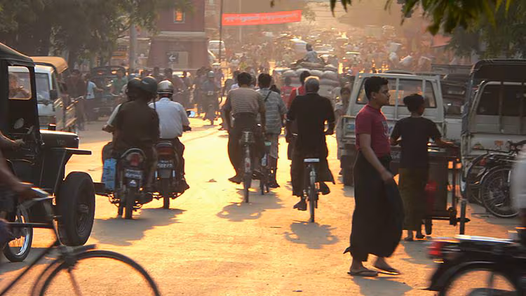 People walking and riding bicycles on a busy street in Mandalay