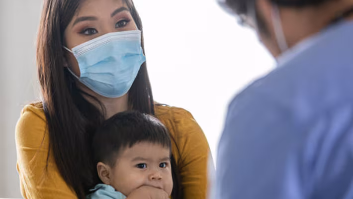 Mom holding child at doctor's office Masked mom holds her child in front of a doctor at an appointment.