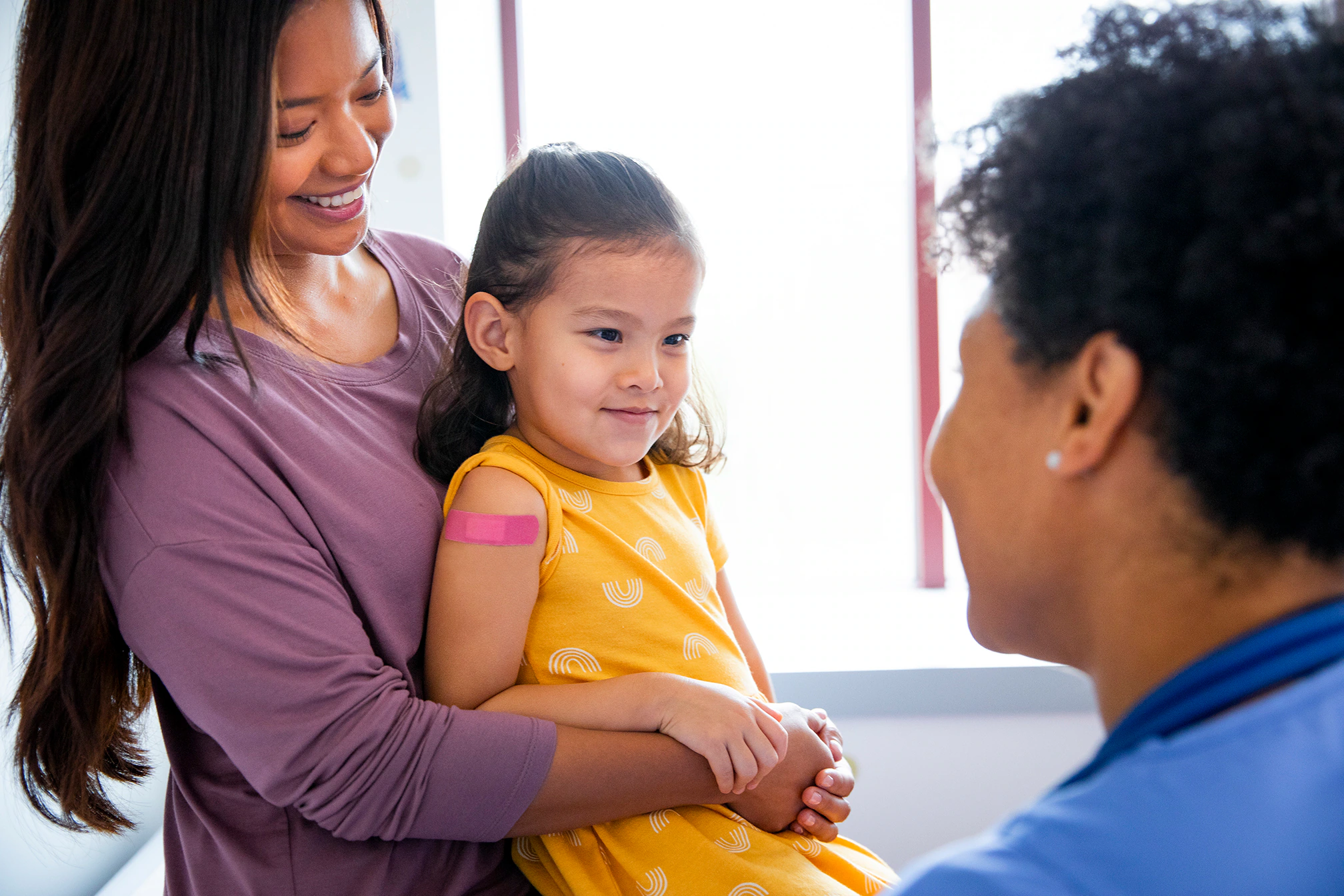 Pediatric patient and parent with healthcare provider Pediatric patient with band-aid on upper arm sitting with parent talking to healthcare provider in a medical office.