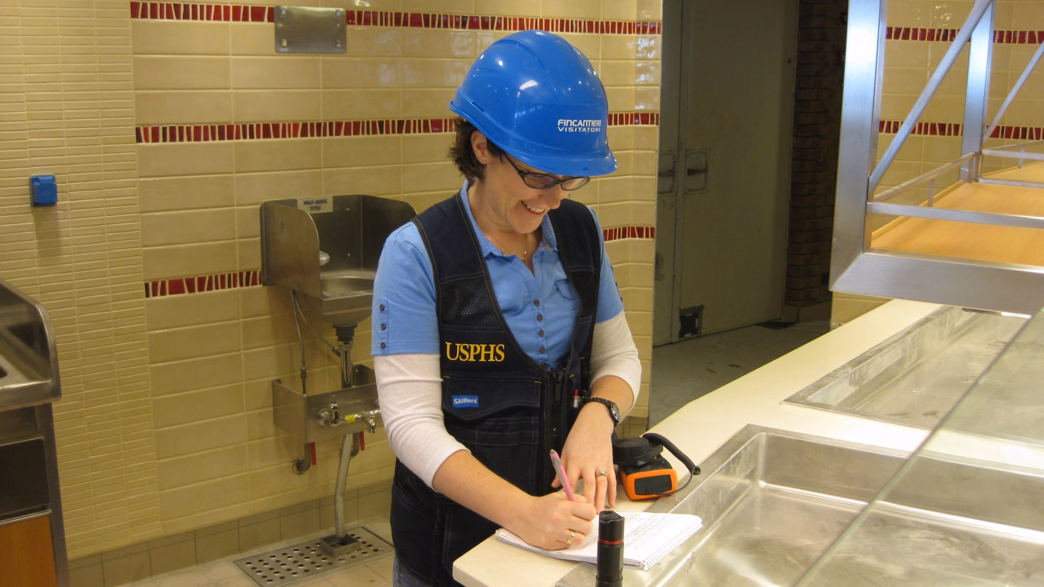 Construction inspections Public health officer wearing a hard hat taking notes on a clipboard inside a galley.