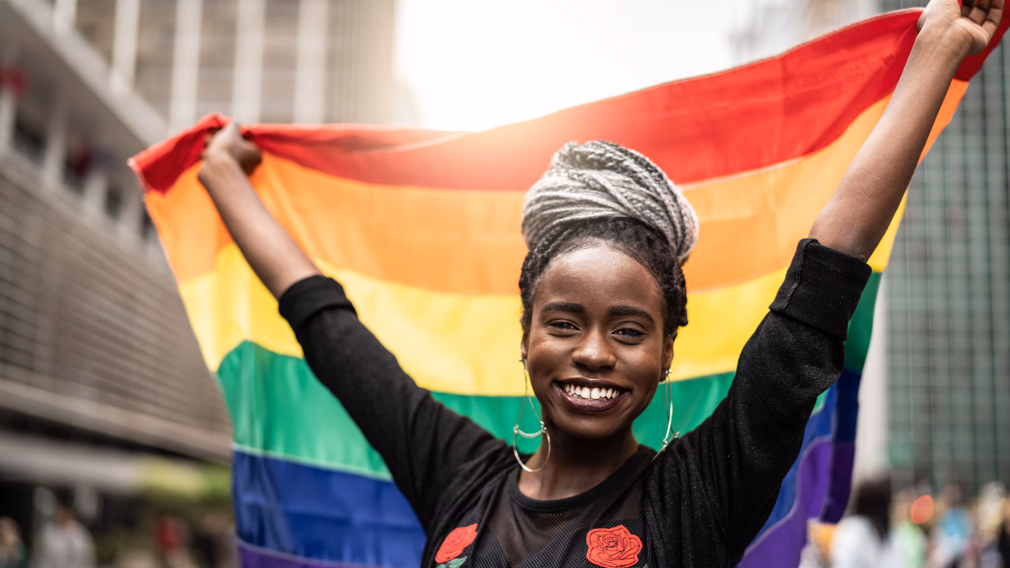 Young woman holds up a rainbow flag behind her head.